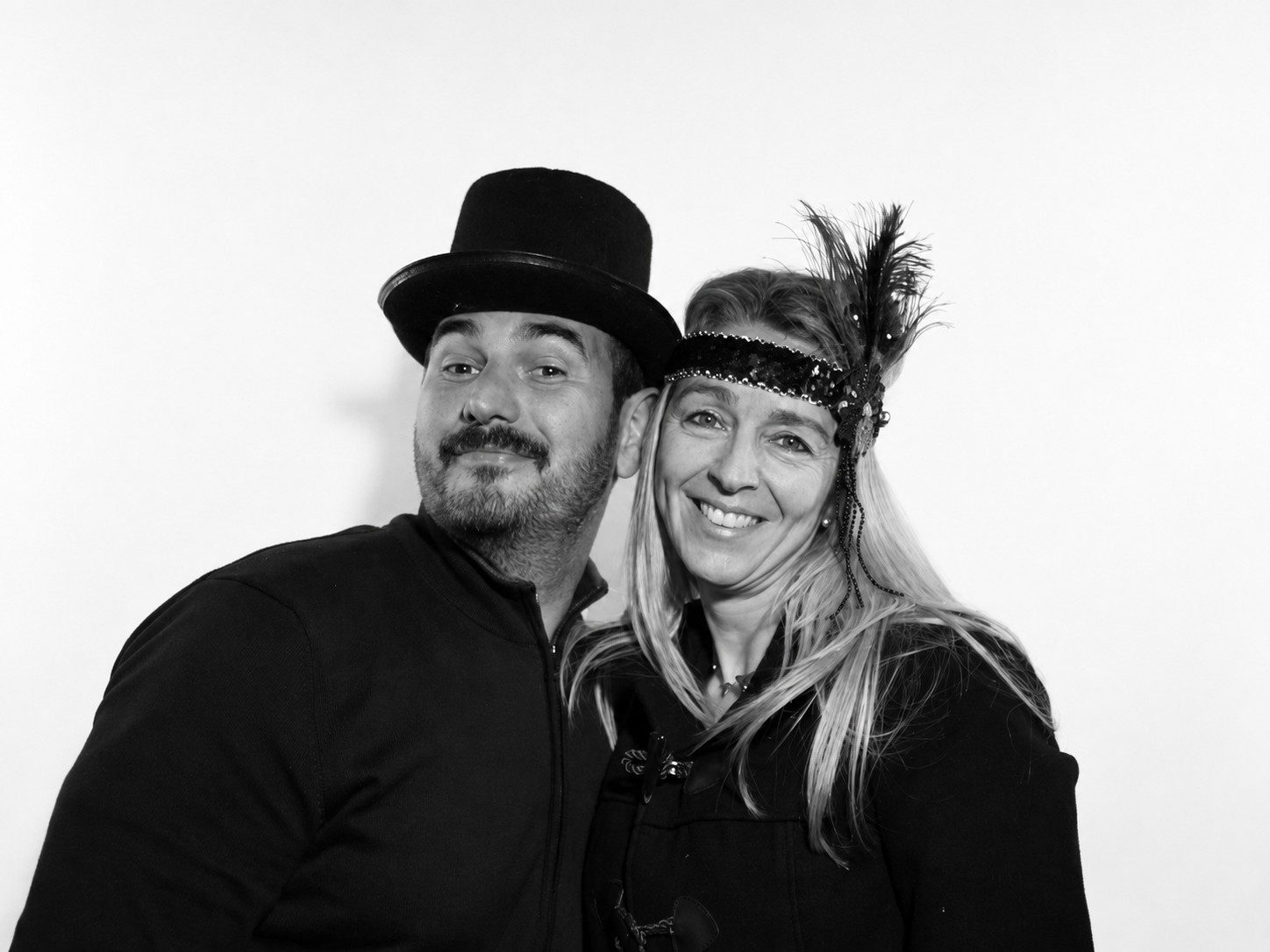 FOTOMATON BLACK & WHITE 2 Pareja de invitados sonriendo con sombrero y accesorio de plumas en Black & White