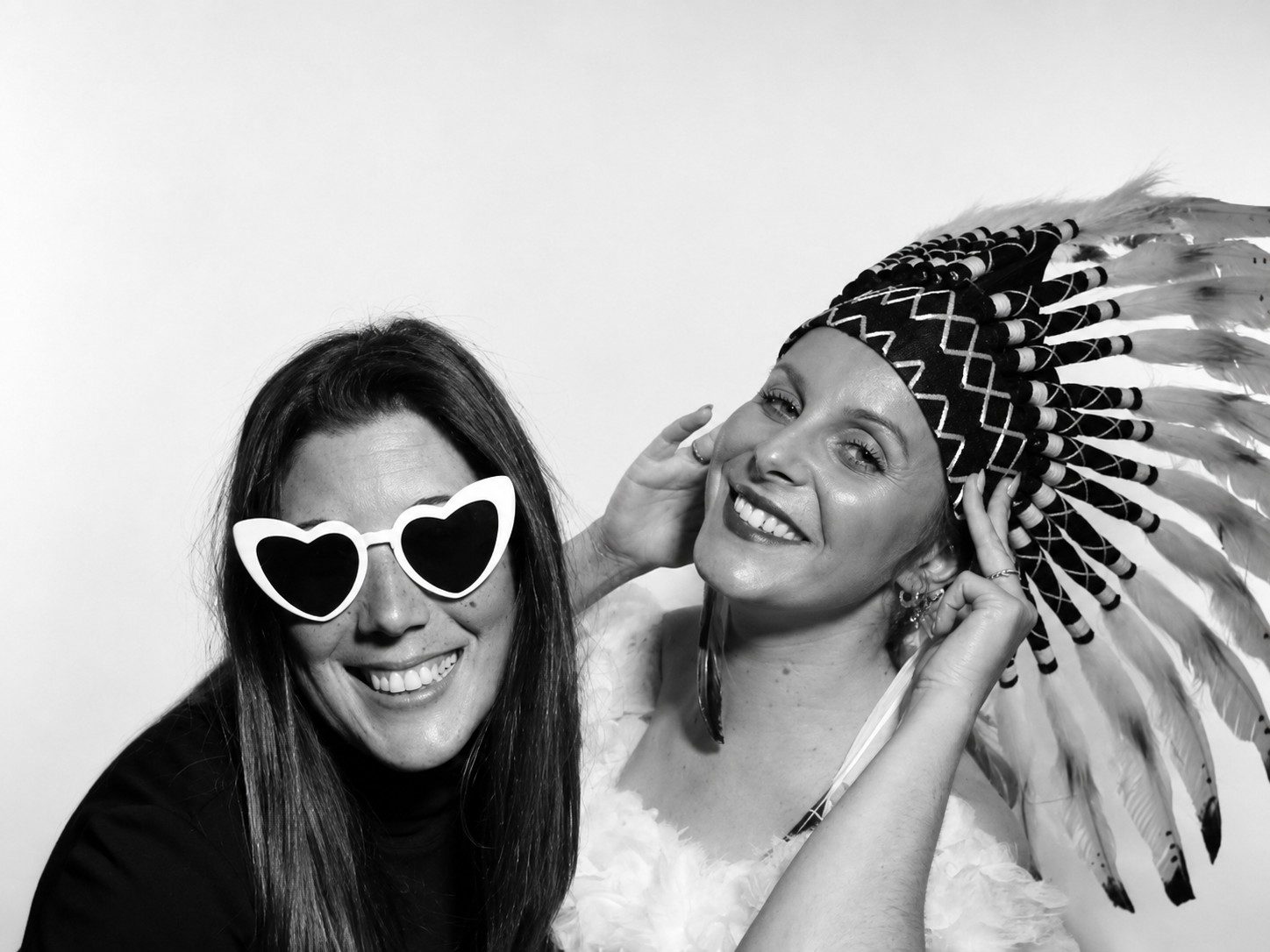 FOTOMATON BLACK & WHITE 6 Dos invitadas sonriendo con gafas de corazón y accesorio de plumas